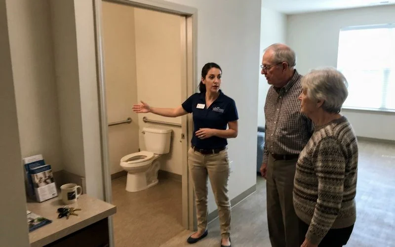 An adult child and an older parent walking through a senior apartment community clubhouse during a tour